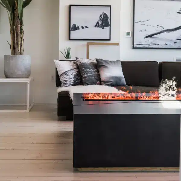Modern living room with a dark sectional sofa, nature-themed pillows, framed wall art, a large potted plant, and a rectangular electric fireplace with visible flames.