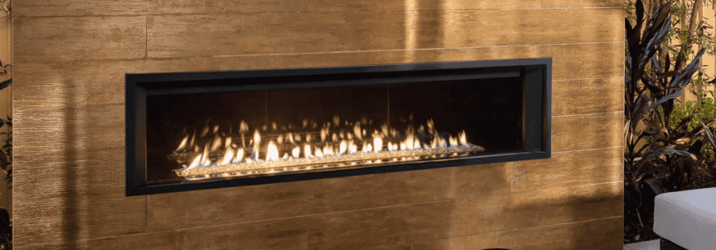 Rectangular modern gas fireplace with a wide black frame set in a brown tile wall, emitting yellow and orange flames—ideal for elevating outdoor living spaces with fireplace warmth and style.